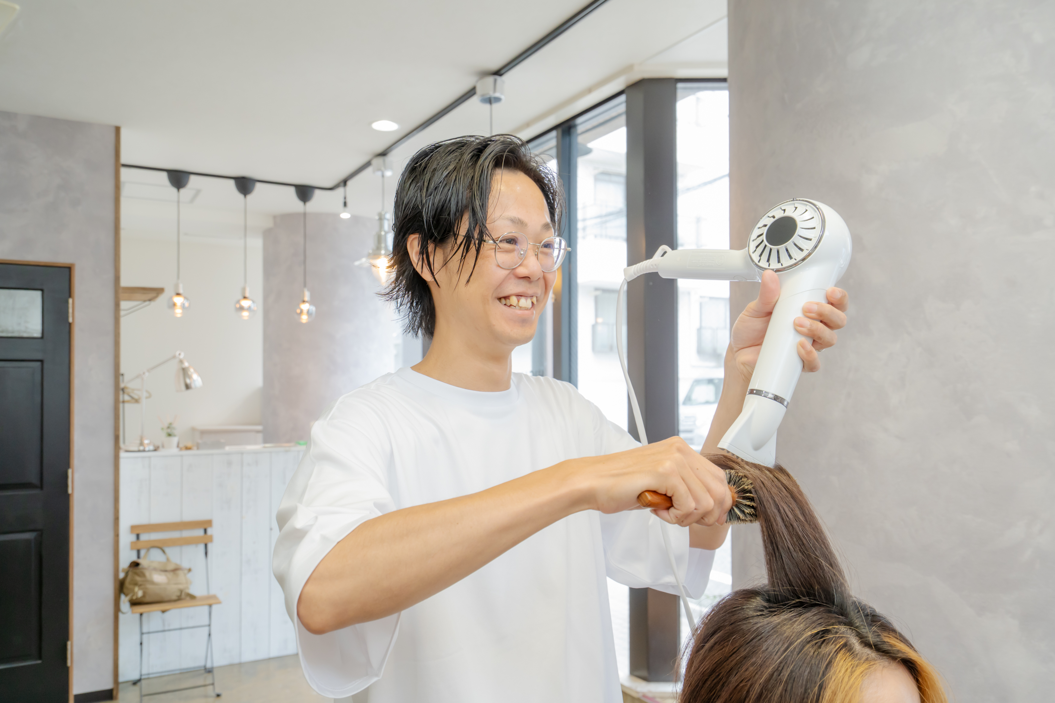 女性の髪を毛流れに合わせてカットするスタイリスト、まとまりやすいシルエットを作る施術シーン